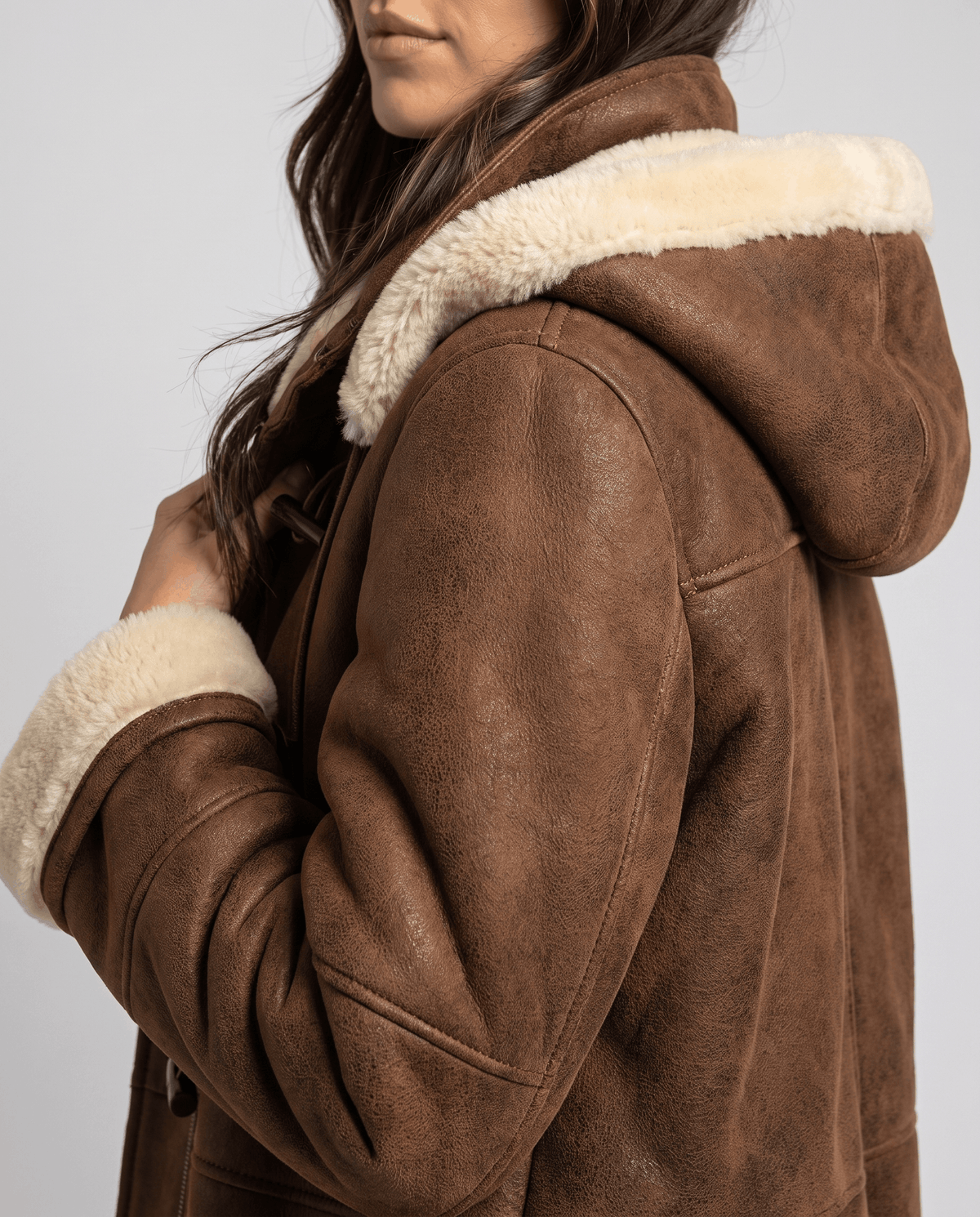 Close-up of a woman wearing a dark brown shearling duffle coat, showing the hood and plush lining