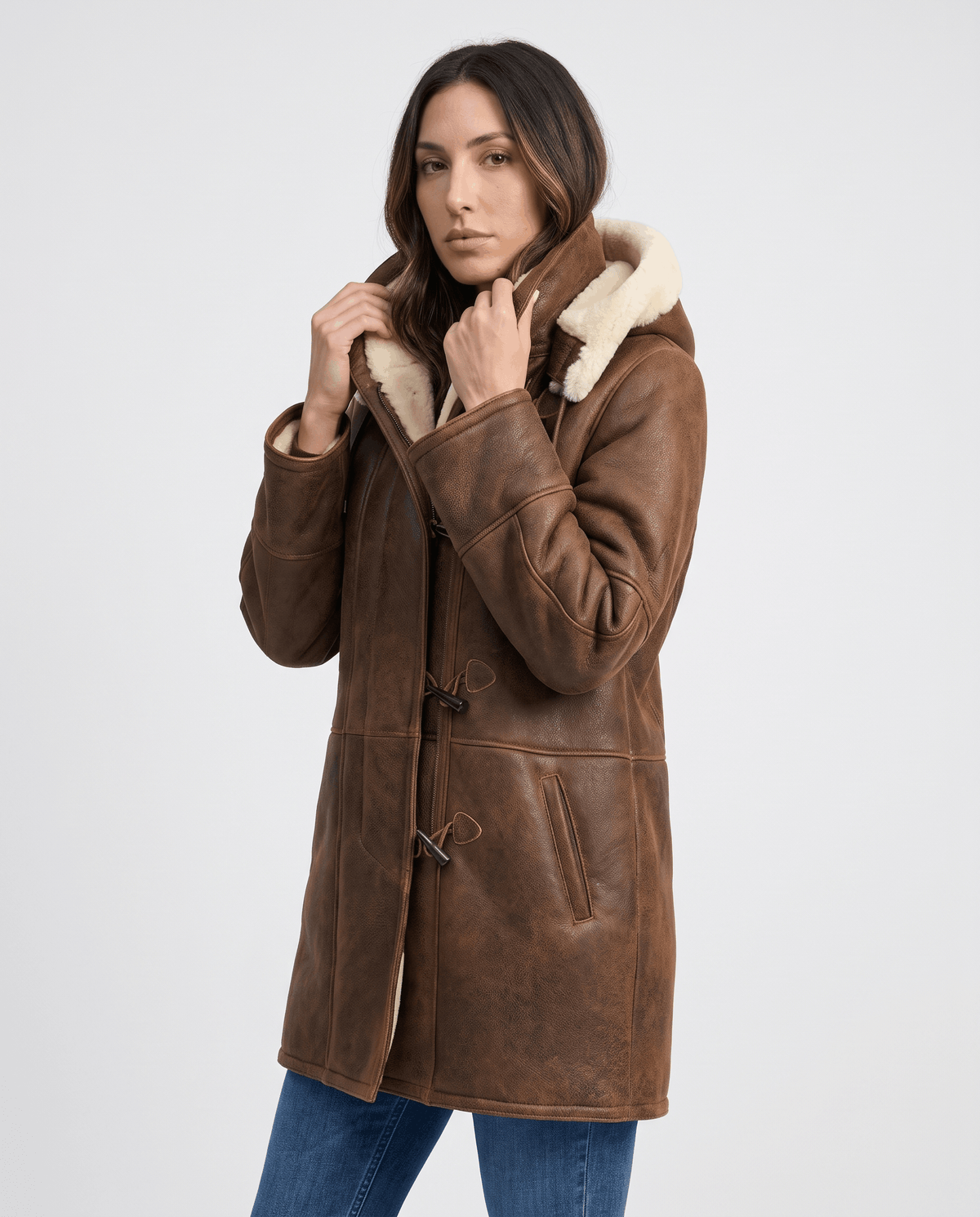 A woman wearing a dark brown shearling duffle coat with a hooded design and toggle zip closure