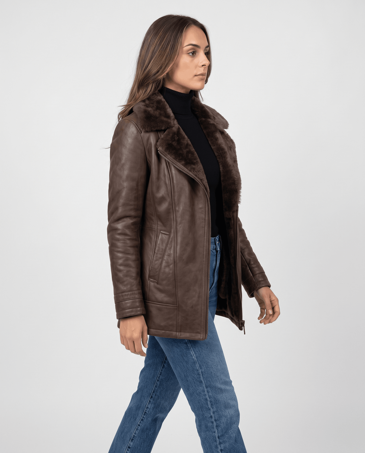 A woman wearing a dark brown shearling leather jacket with an oversized collar and full-zip front, shown in side view