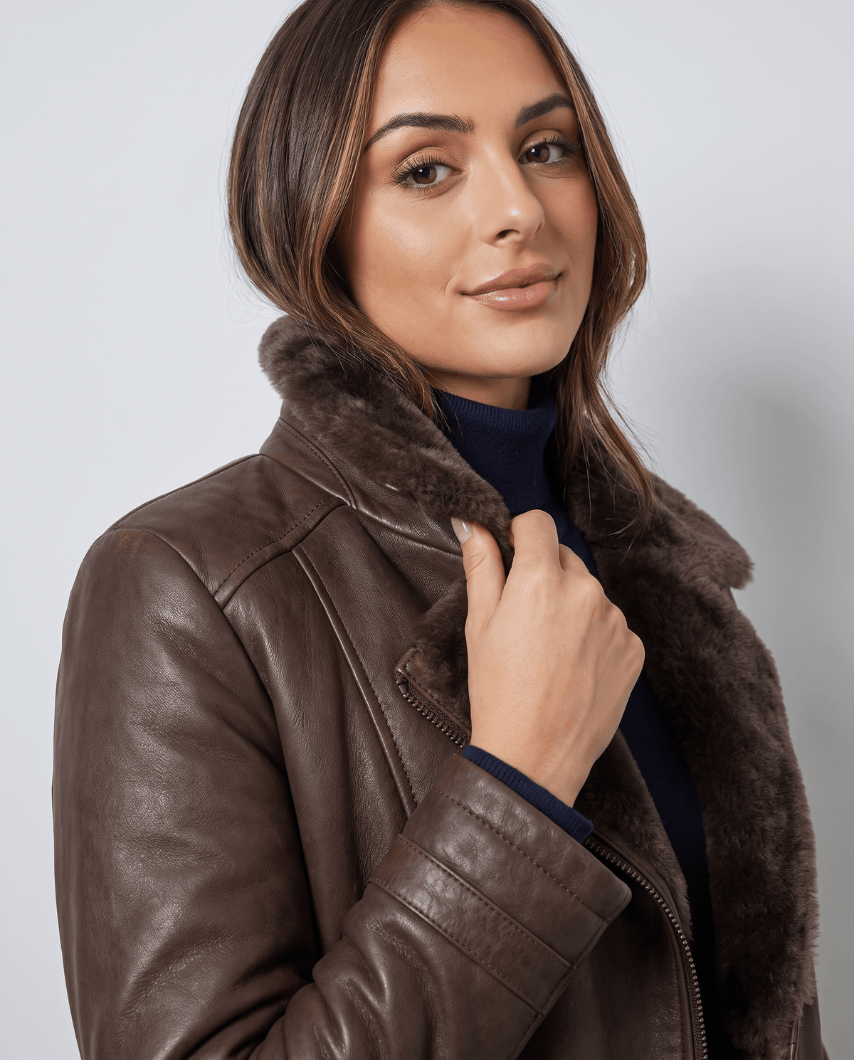 Close-up of a woman wearing a dark brown shearling leather jacket, showing the oversized collar and zip front