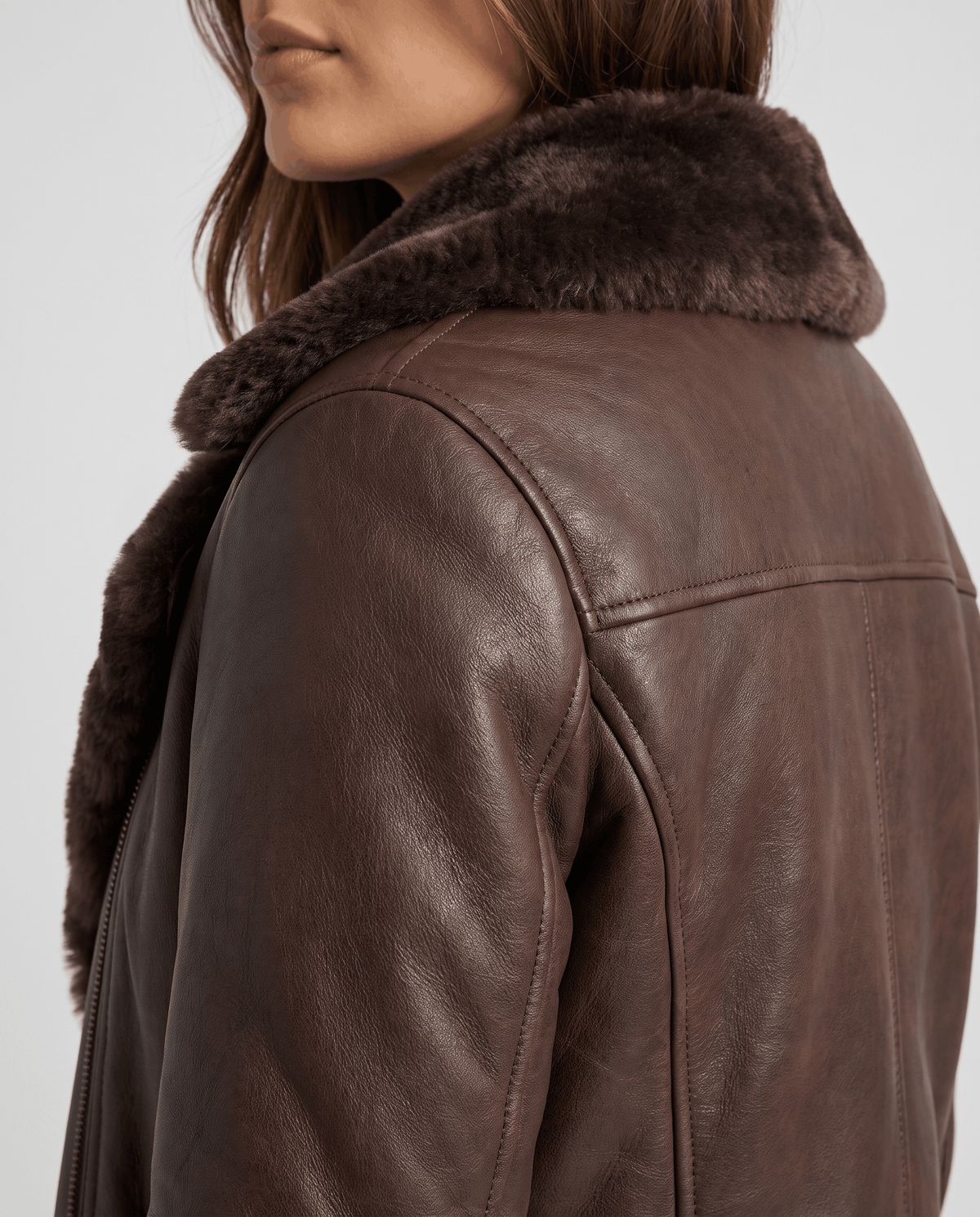Close-up of a brown shearling leather jacket showing the oversized collar, textured lining, and back detail