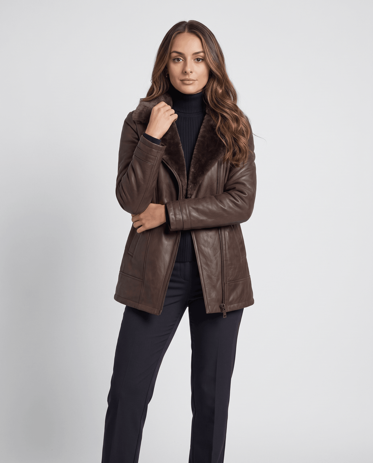 A woman wearing a dark brown shearling leather jacket with an oversized collar and full-zip front, standing indoors