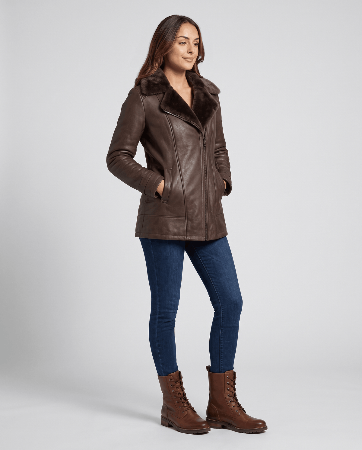 A woman wearing a brown shearling leather jacket with an oversized collar and full-zip front, standing in a three-quarter view