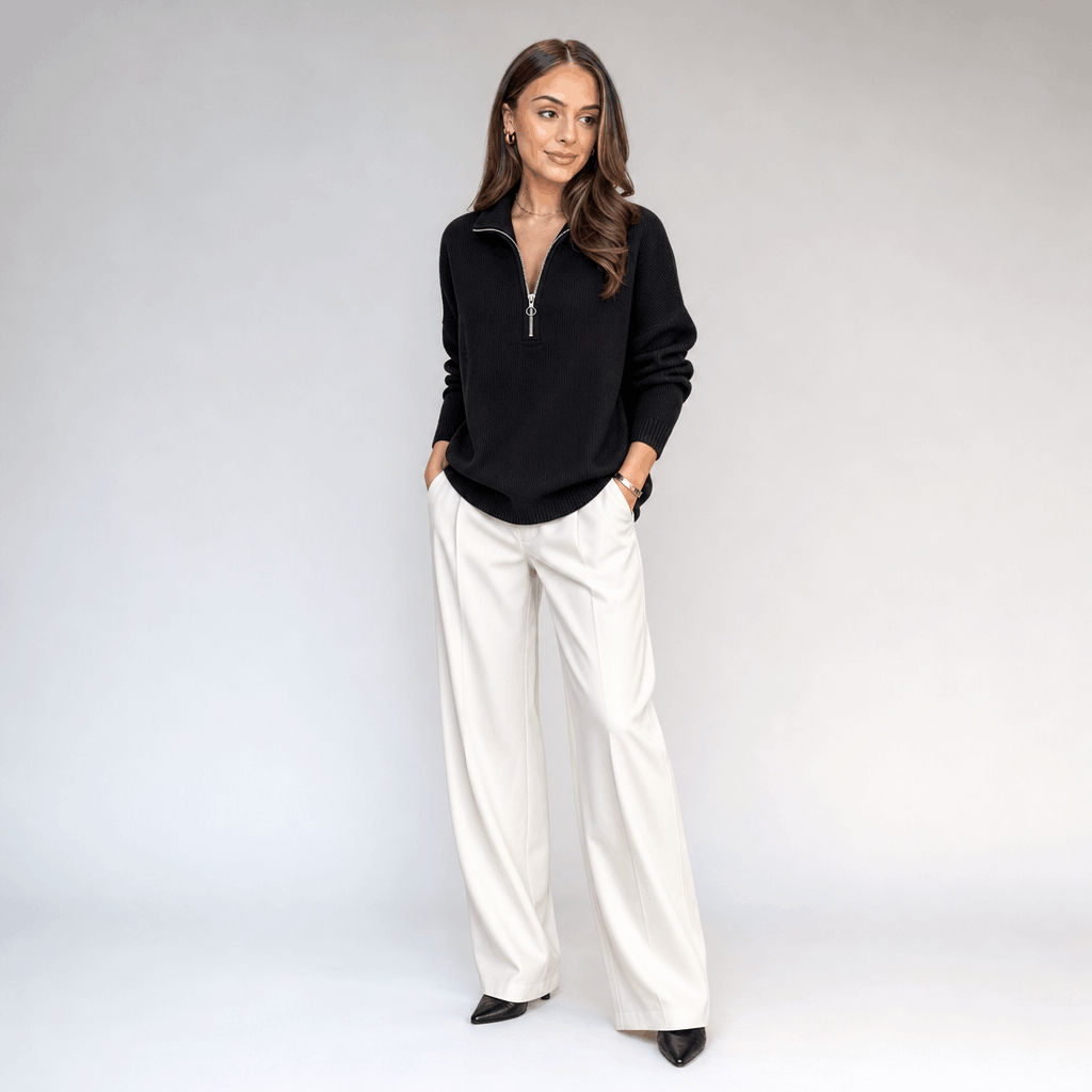 Full-body view of the woman wearing the black ribbed half-zip sweater with white pants.
