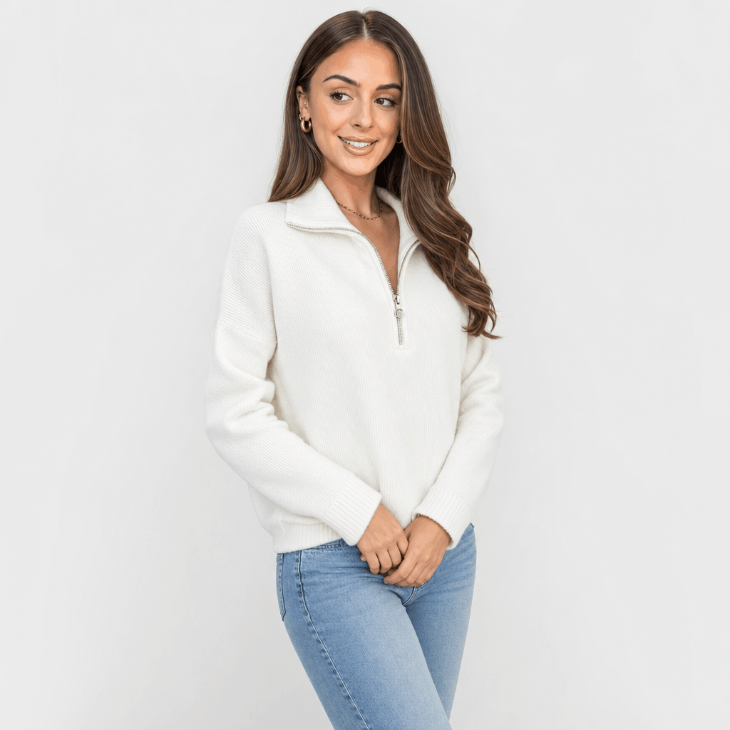 Woman wearing a cream ribbed half-zip sweater with blue jeans, shown in a relaxed standing pose.