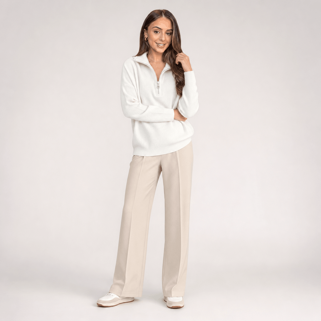 Full-body view of the woman wearing the cream ribbed half-zip sweater with light-colored pants.