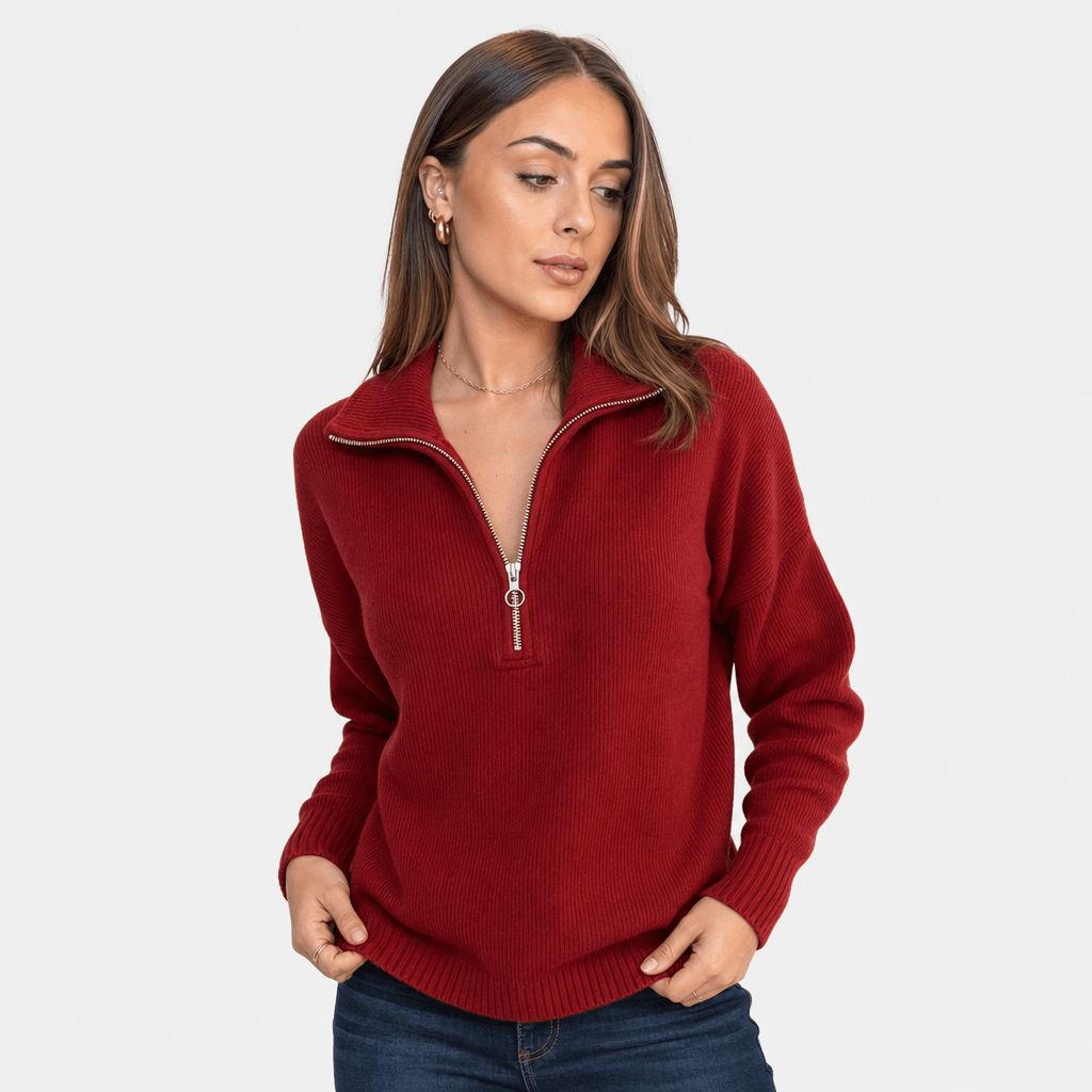 Woman wearing a burgundy red ribbed half-zip sweater with blue jeans, shown in a relaxed pose.