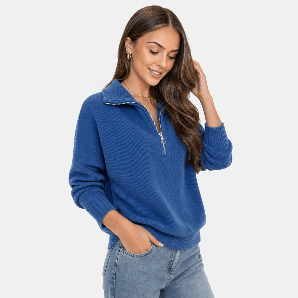 Woman wearing a royal blue ribbed half-zip sweater with blue jeans, shown in a relaxed close-up pose.