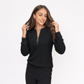 Woman wearing a black ribbed half-zip sweater with fitted black pants, shown adjusting her collar.
