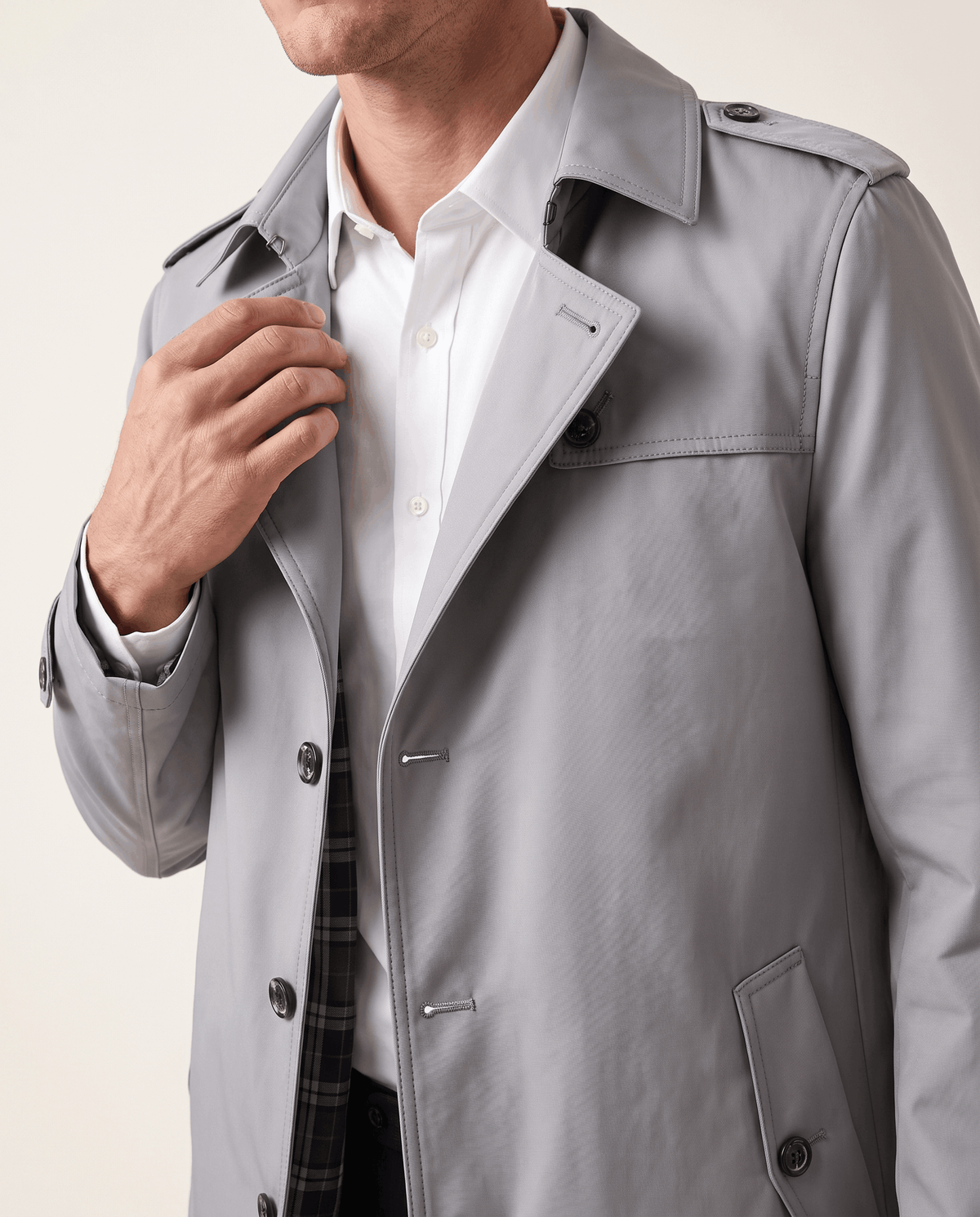 A man wearing a light gray single-breasted trench coat with structured lapels and a tailored fit, close-up view