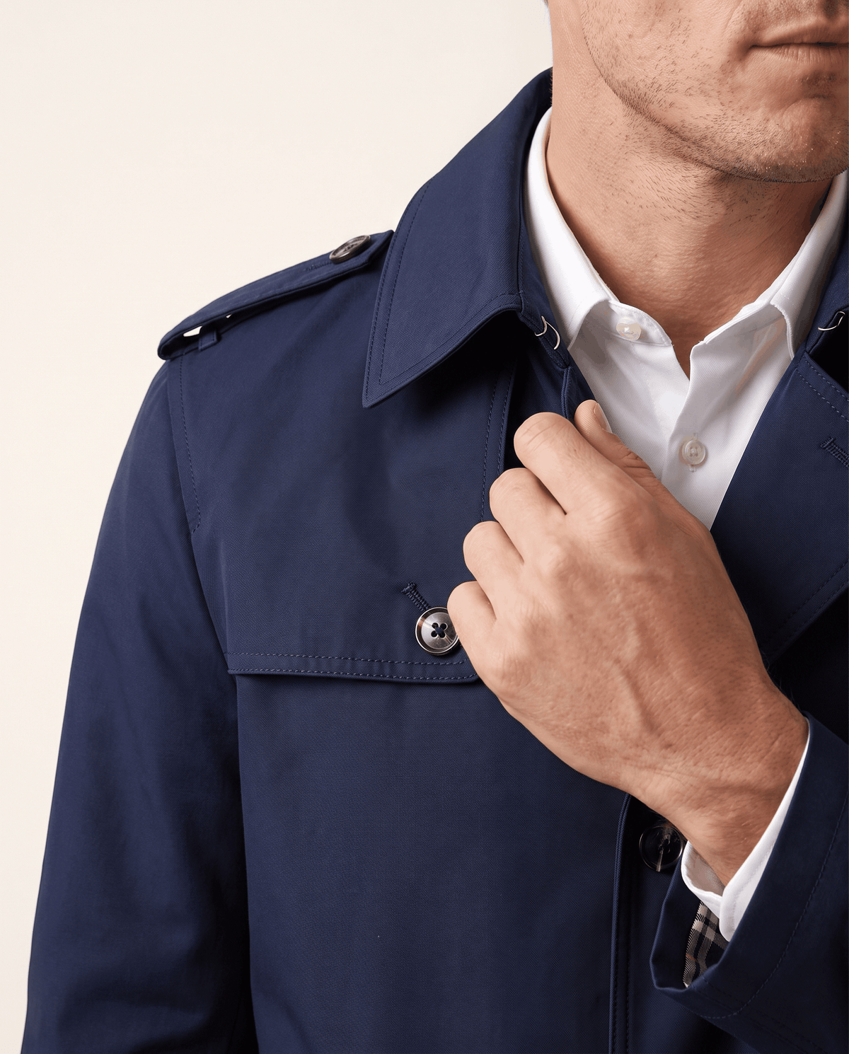 Close-up of a man wearing a navy blue single-breasted trench coat, showing the structured lapel and shoulder detail
