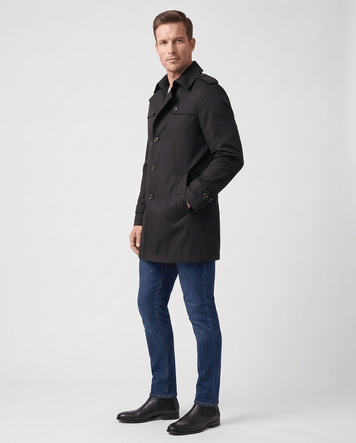 A man wearing a black single-breasted trench coat with a mid-length fit, structured lapels, and tailored silhouette, side view