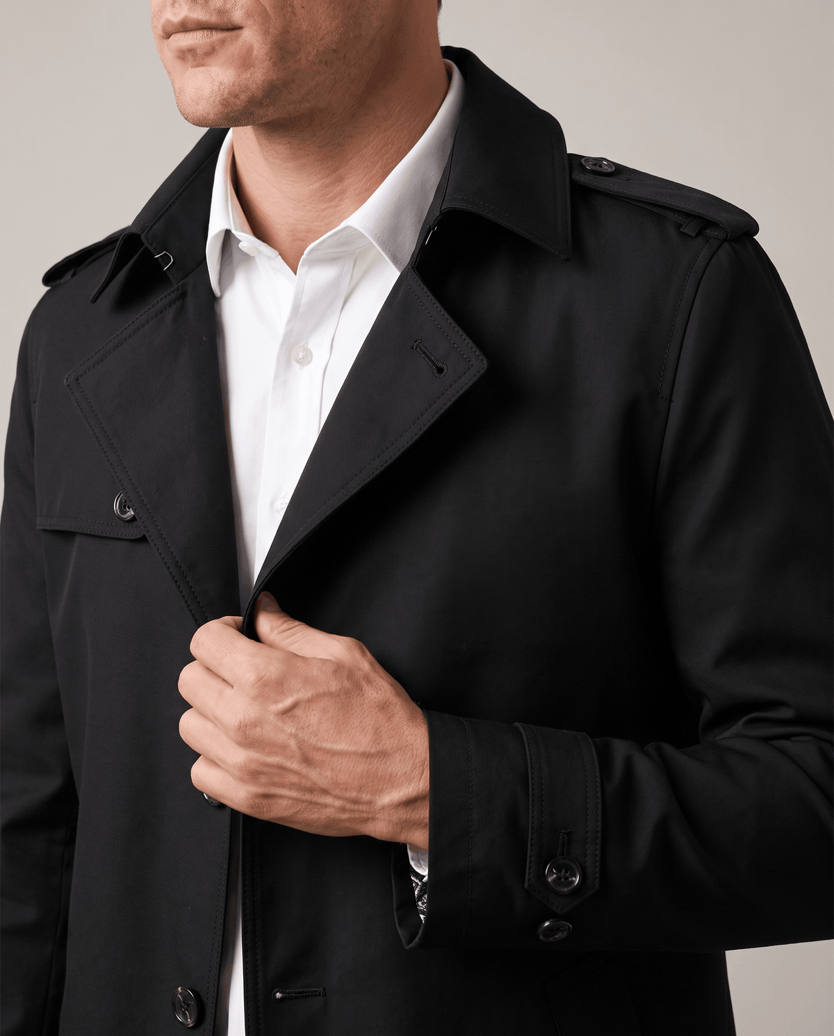 Close-up of a man wearing a black single-breasted trench coat, showing the structured lapel and button front
