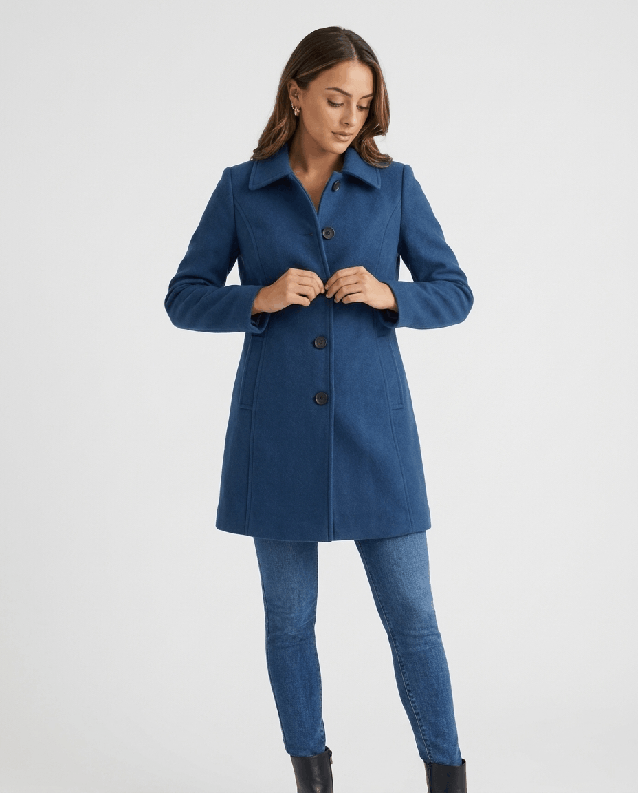 A woman wearing a blue single-breasted mid-length trench coat with a button front and tailored fit