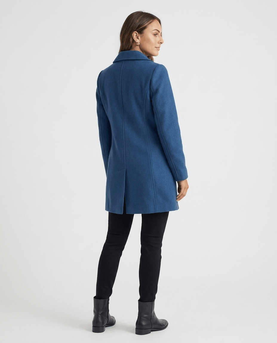 A woman wearing a blue single-breasted mid-length trench coat, shown from the back