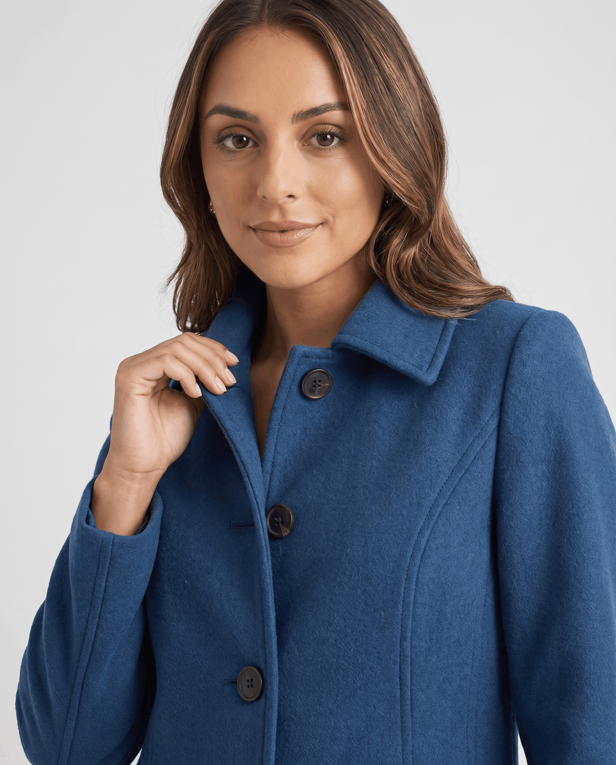 Close-up of a woman wearing a blue single-breasted mid-length trench coat, showing the lapel collar and button front