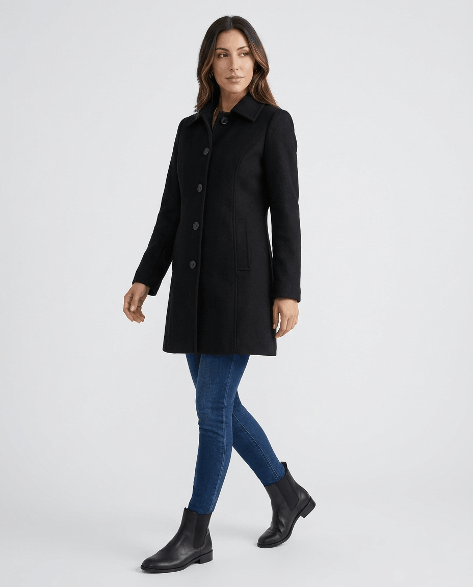 A woman wearing a black single-breasted mid-length trench coat with a button front and tailored fit