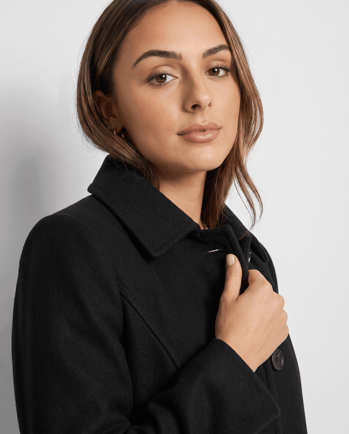 Close-up of a woman wearing a black single-breasted mid-length trench coat, showing the lapel collar and button front