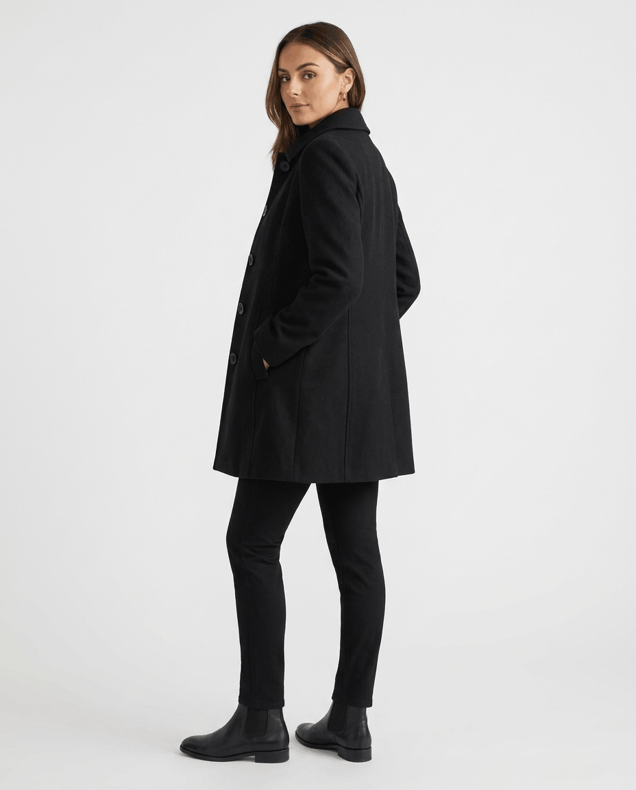 A woman wearing a black single-breasted mid-length trench coat, shown from the back