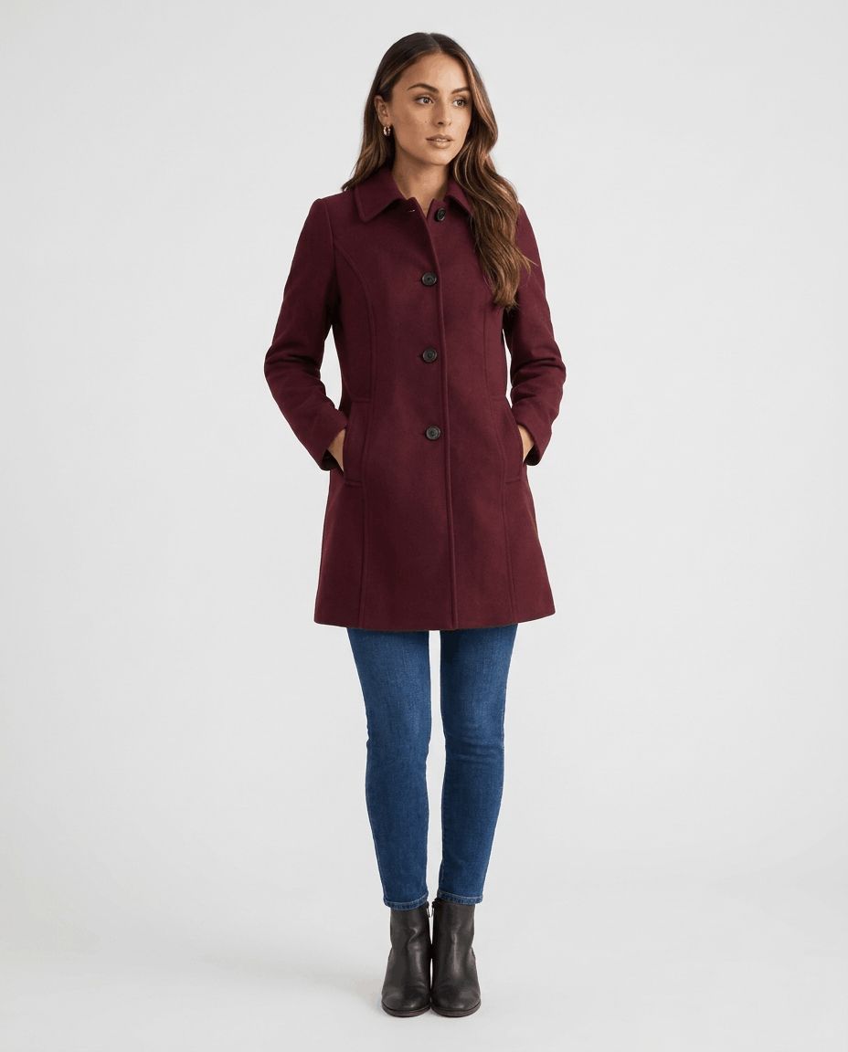 A woman wearing a burgundy single-breasted mid-length trench coat with a button front and tailored fit