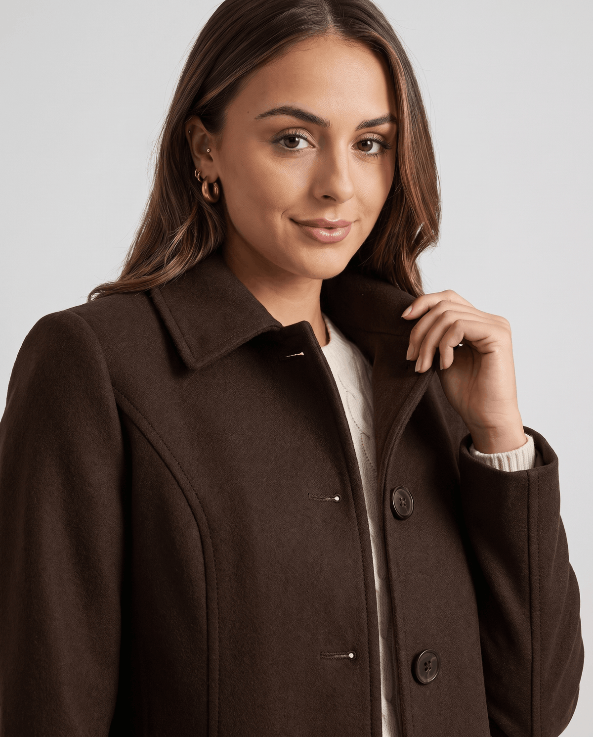 Close-up of a woman wearing a dark brown single-breasted mid-length trench coat, showing the lapel collar and button front