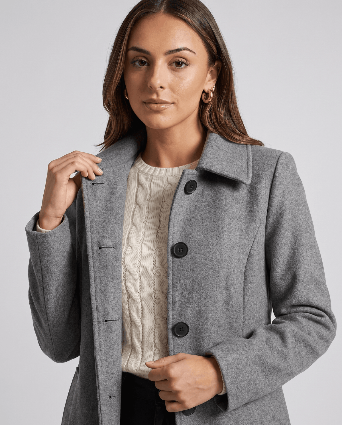 A woman wearing a gray single-breasted mid-length trench coat with a lapel collar and button front, close-up view