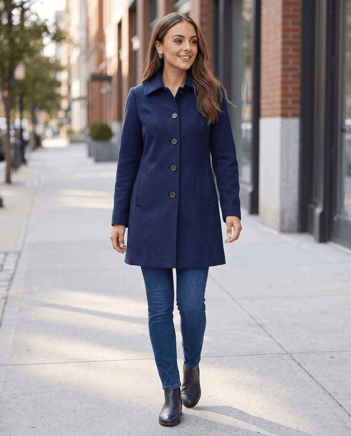 A woman wearing a blue single-breasted mid-length trench coat with a button front, walking outdoors