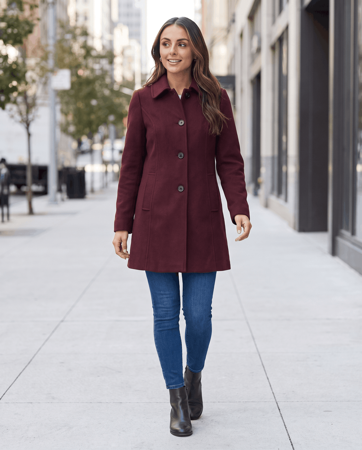 A woman wearing a burgundy single-breasted mid-length trench coat with a button front, walking outdoors