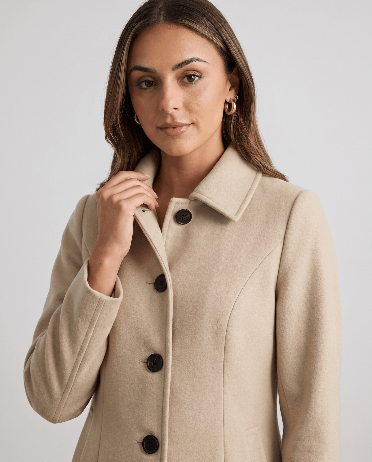 Close-up of a woman wearing a cream single-breasted mid-length trench coat, showing the lapel collar and button front