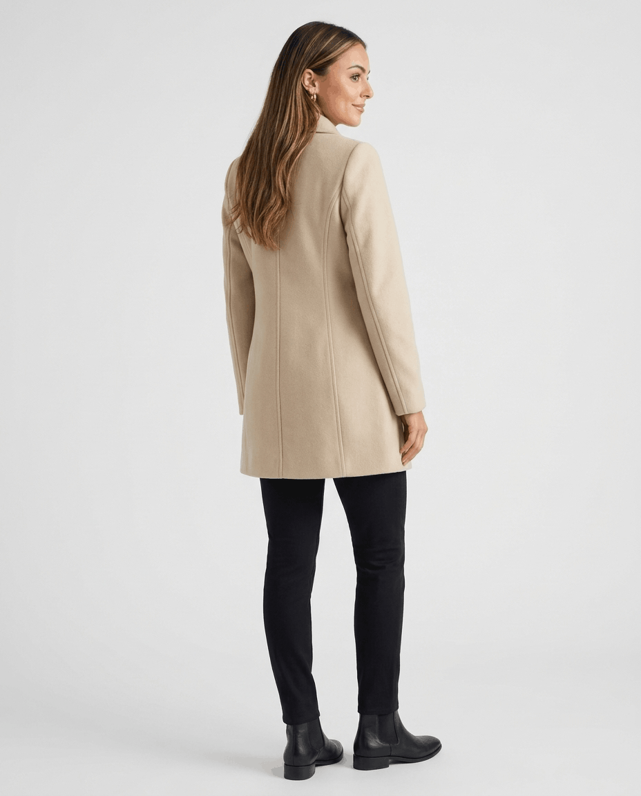 A woman wearing a cream single-breasted mid-length trench coat, shown from the back