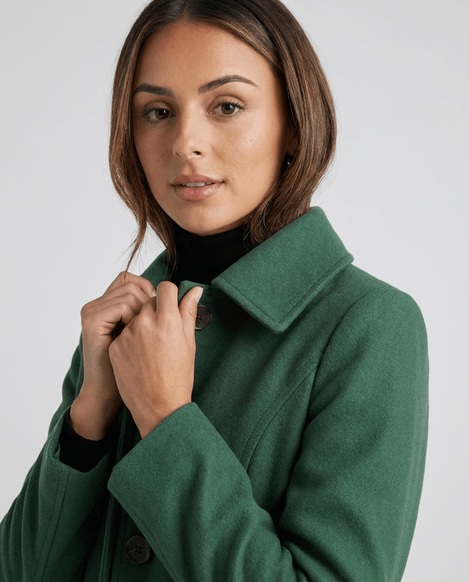 Close-up of a woman wearing a green single-breasted mid-length trench coat, showing the lapel collar and button front