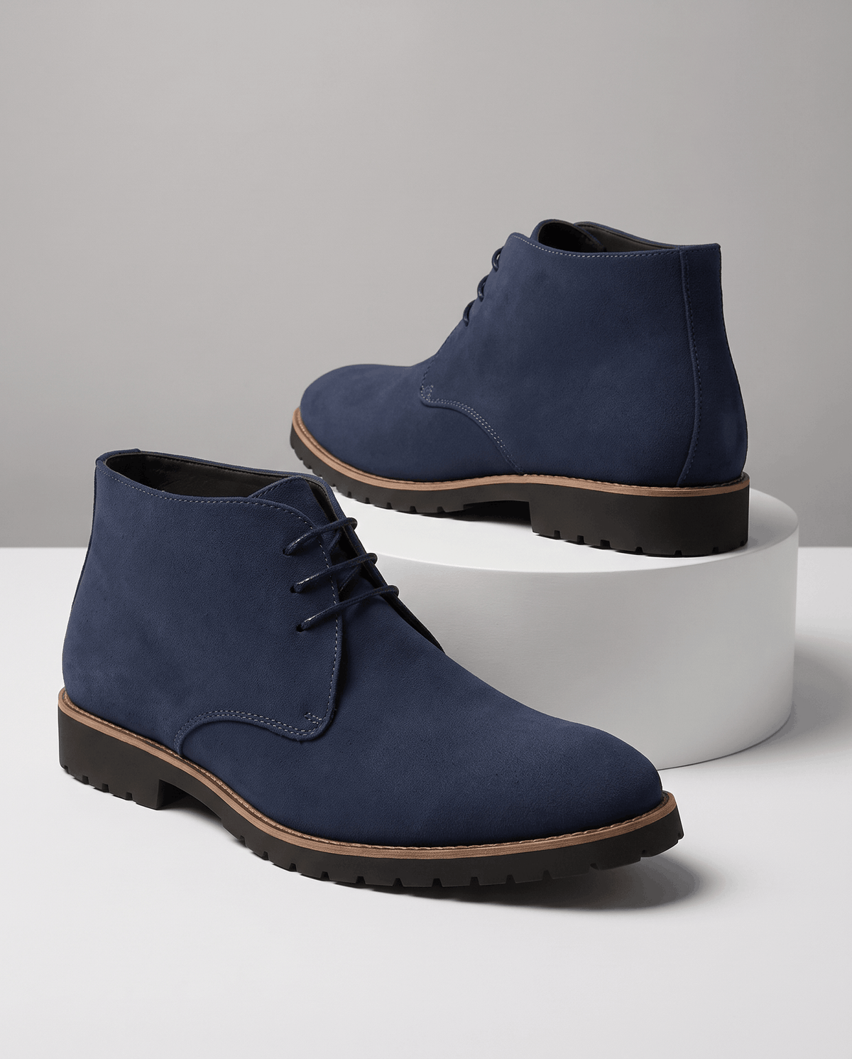 A pair of navy blue suede ankle boots with lug soles and three-eyelet lacing, shown on a display surface