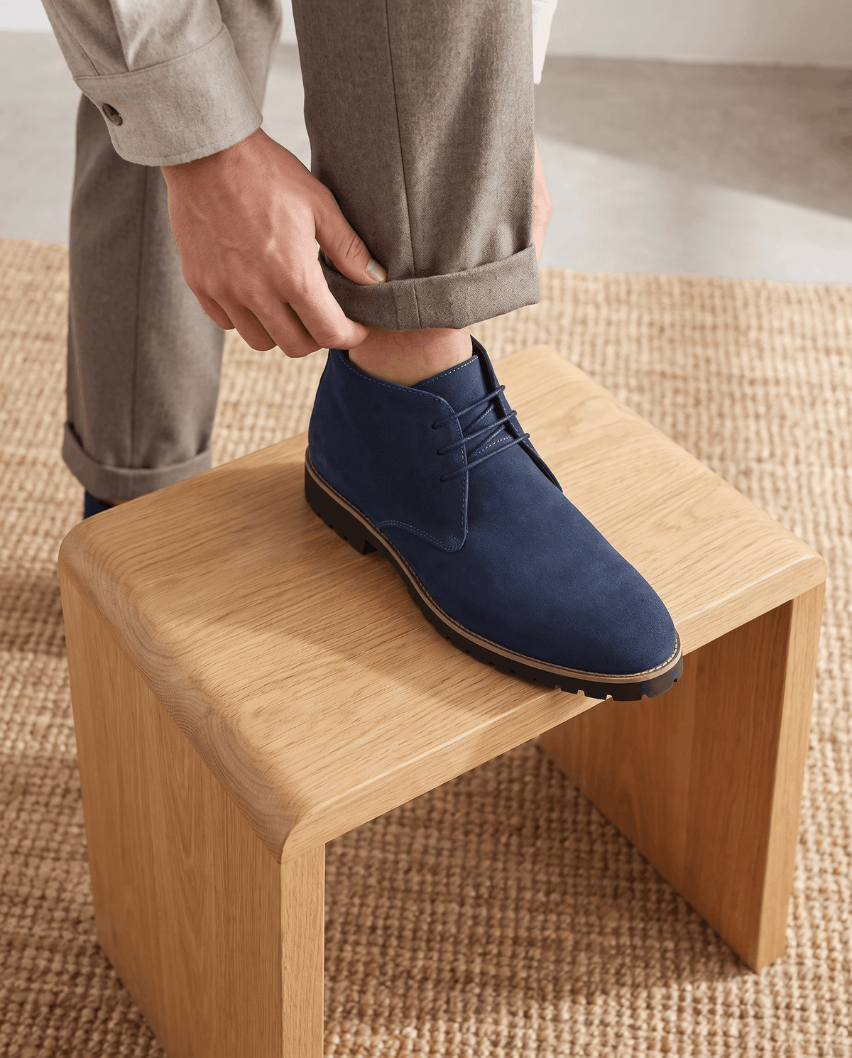 A person putting on a navy blue suede ankle boot with a lug sole and three-eyelet lacing