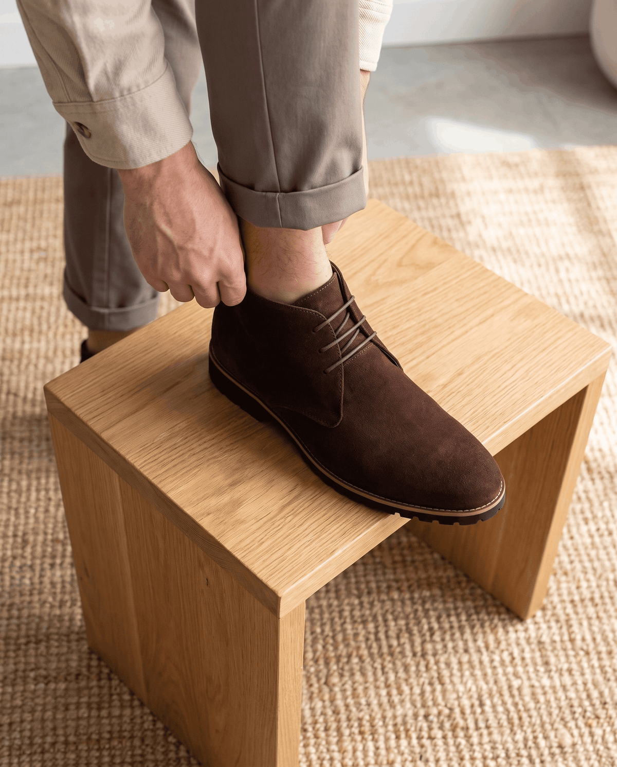 A person wearing brown suede ankle boots with lug soles and three-eyelet lacing