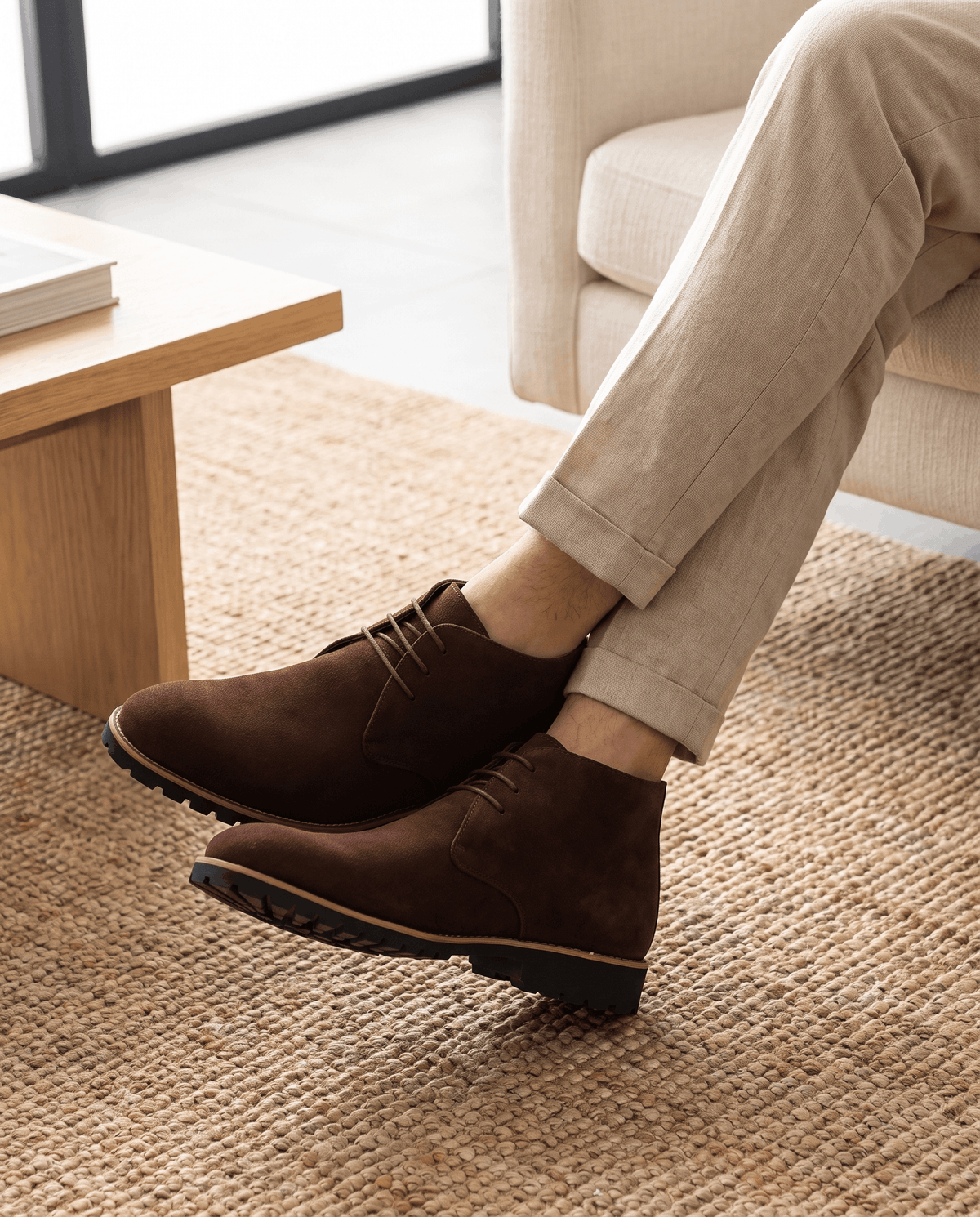 Close-up of a person wearing brown suede ankle boots with lug soles and three-eyelet lacing