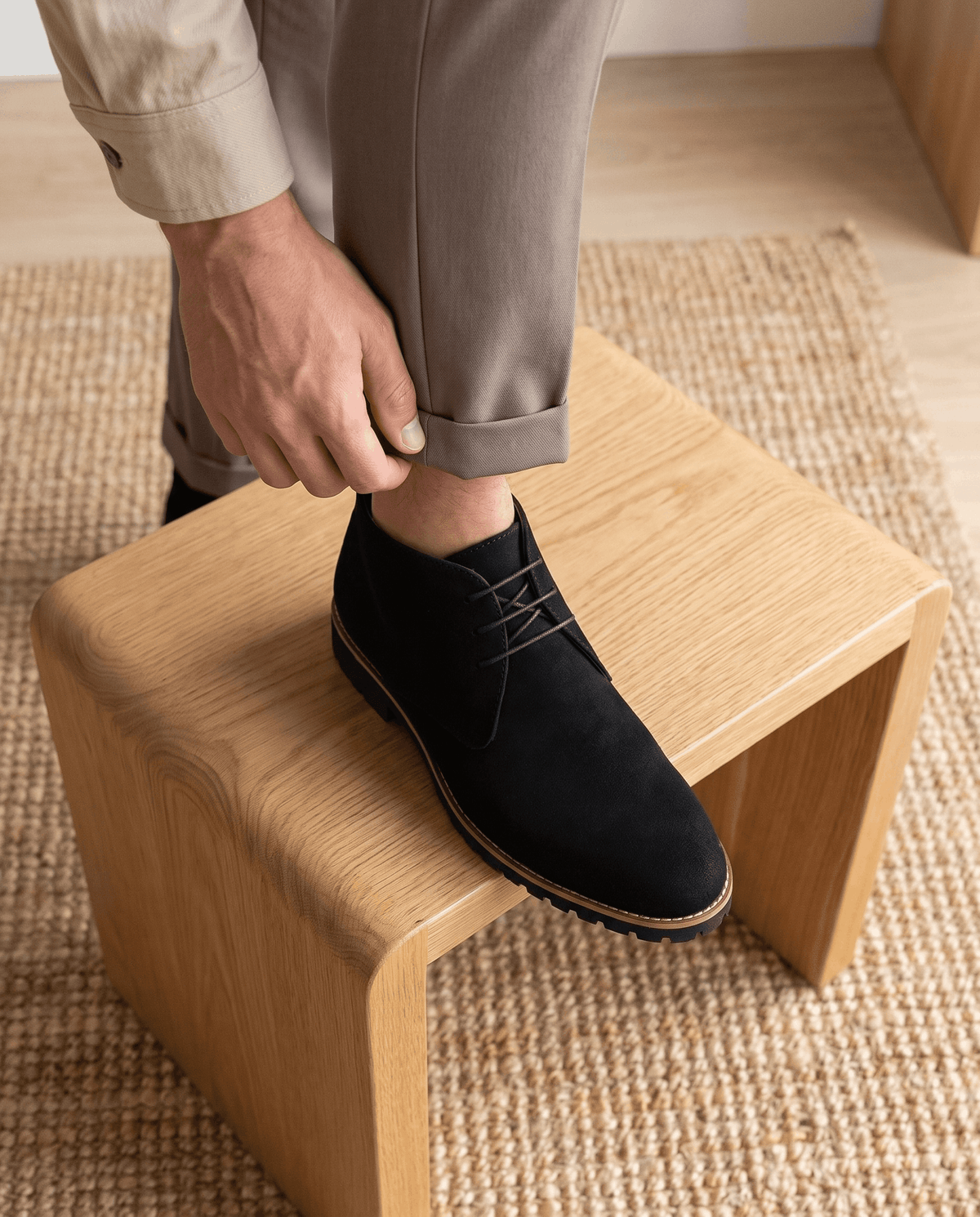 A person putting on black suede ankle boots with lug soles and three-eyelet lacing