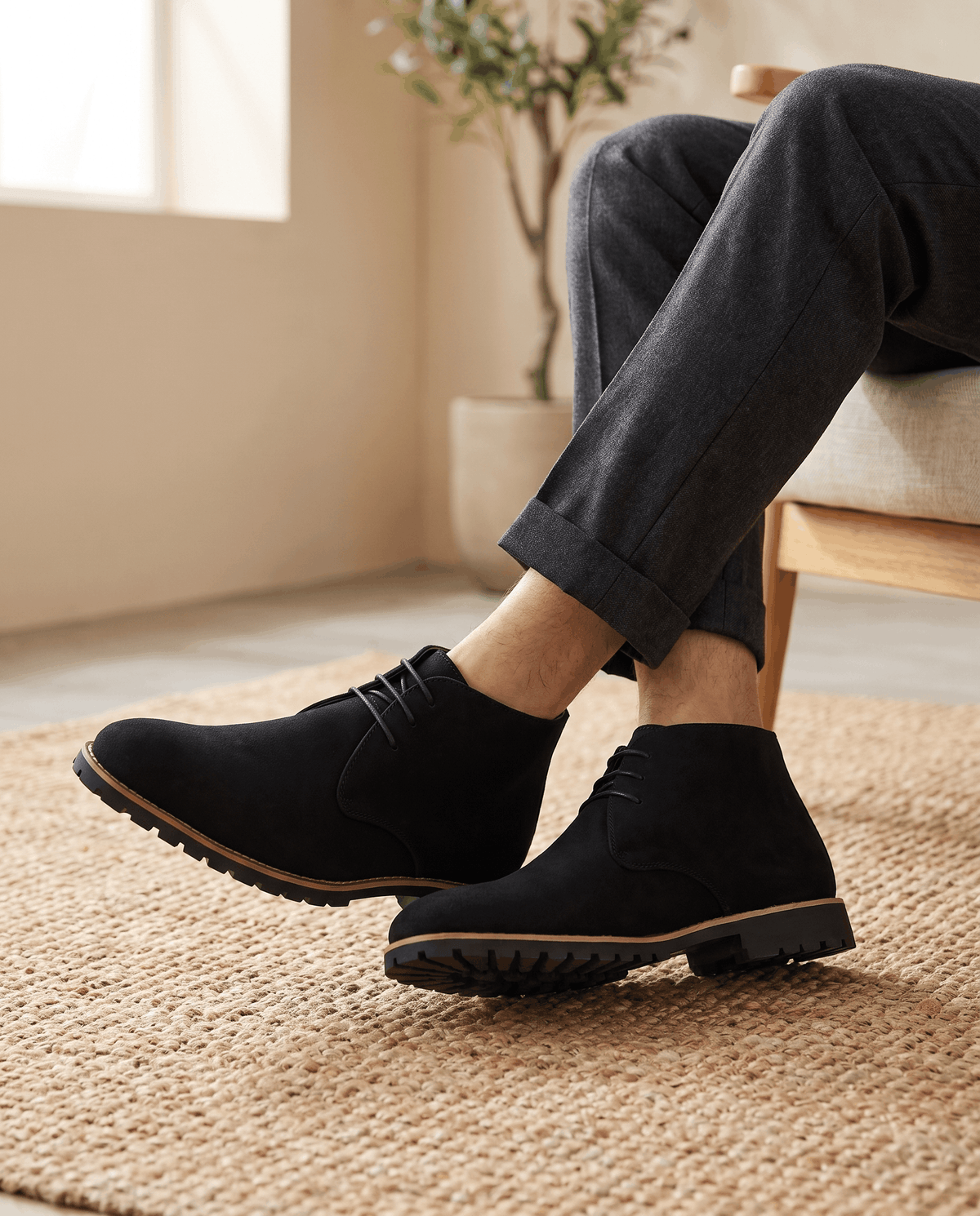 A person wearing black suede ankle boots with lug soles and three-eyelet lacing, seated indoors