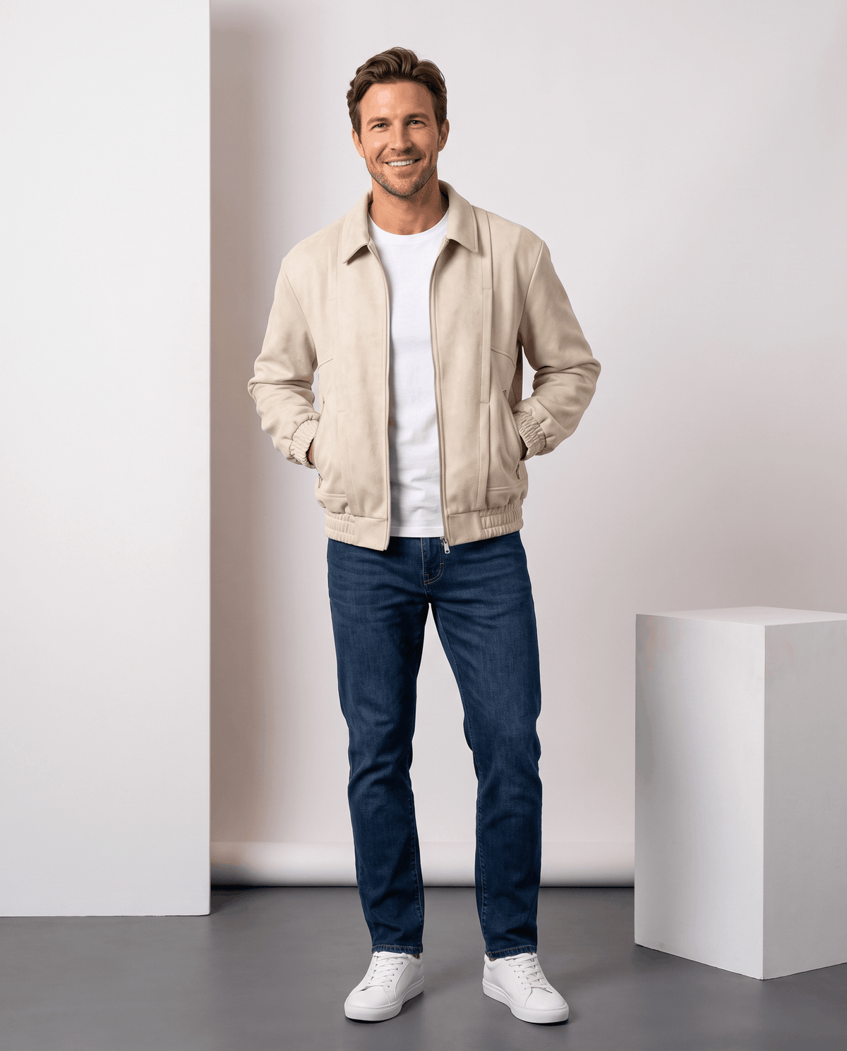 A man wearing a cream suede bomber jacket with a relaxed fit, stand collar, and zip pockets