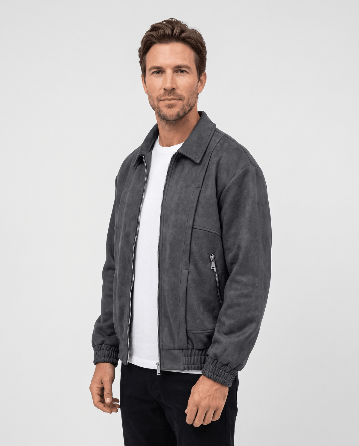 A man wearing a dark gray suede bomber jacket with a relaxed fit and zip pockets