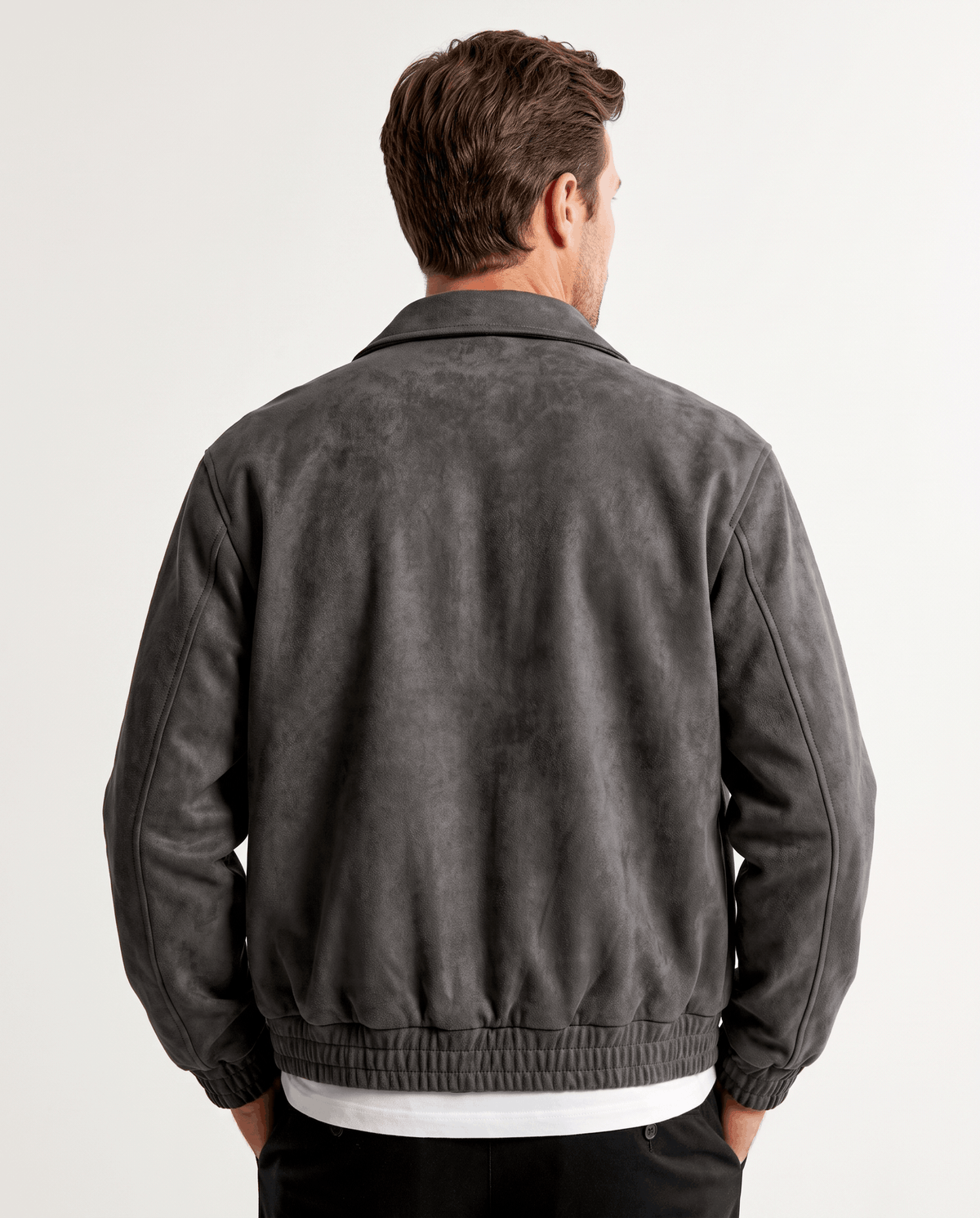 A man wearing a dark gray suede bomber jacket with a relaxed fit, shown from the back