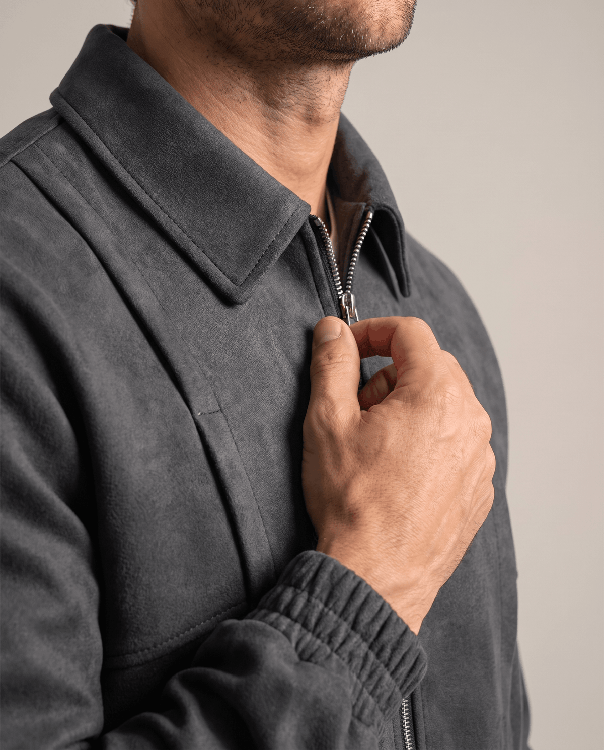 Close-up of a man wearing a dark gray suede bomber jacket, showing the stand collar and front zip closure