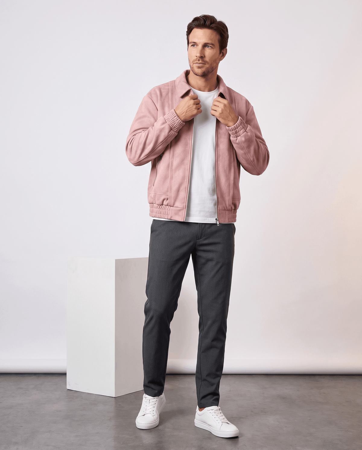A man wearing a pink suede bomber jacket with a relaxed fit and zip pockets, standing indoors