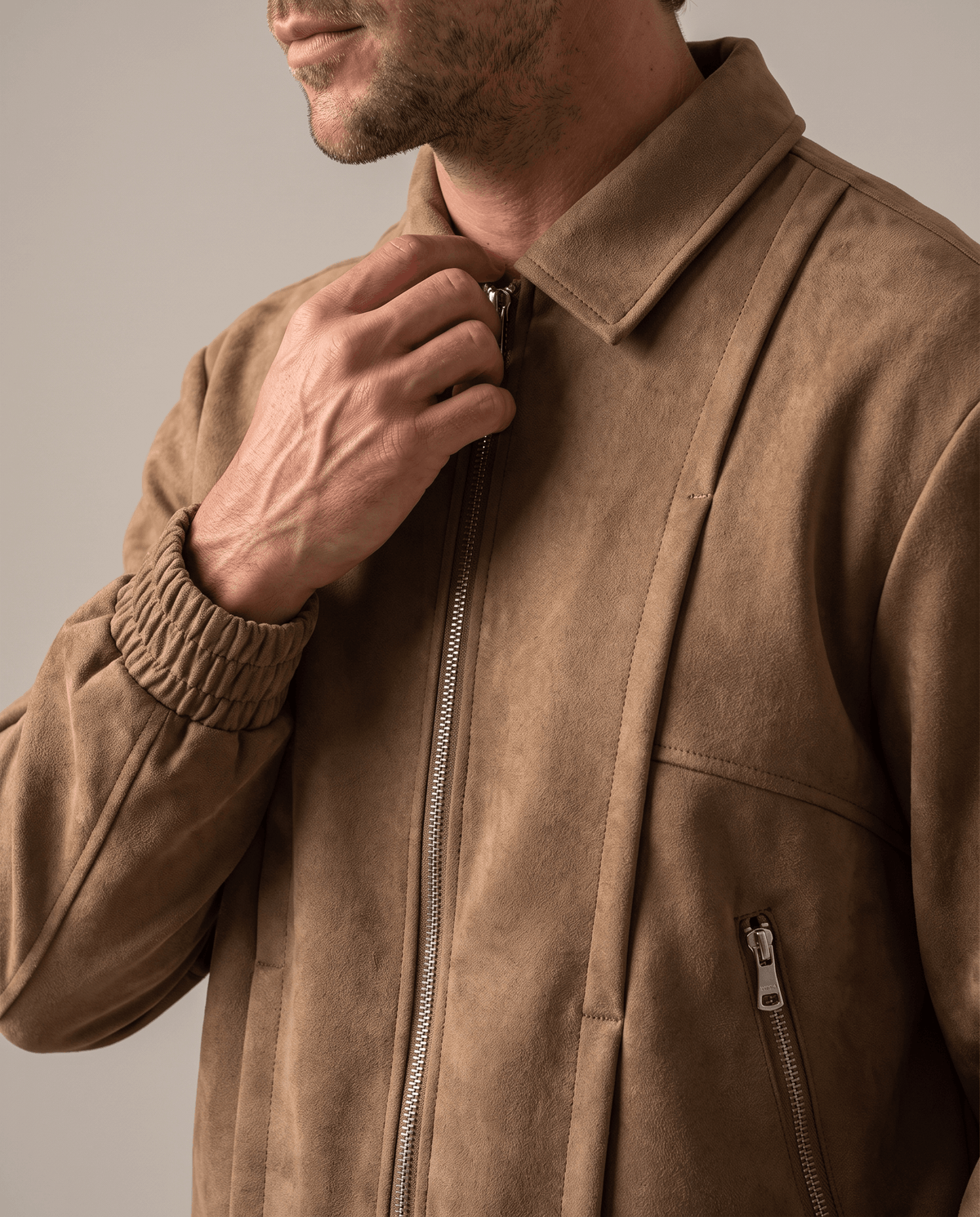 Close-up of a man wearing a brown suede bomber jacket, showing the collar and front zip closure