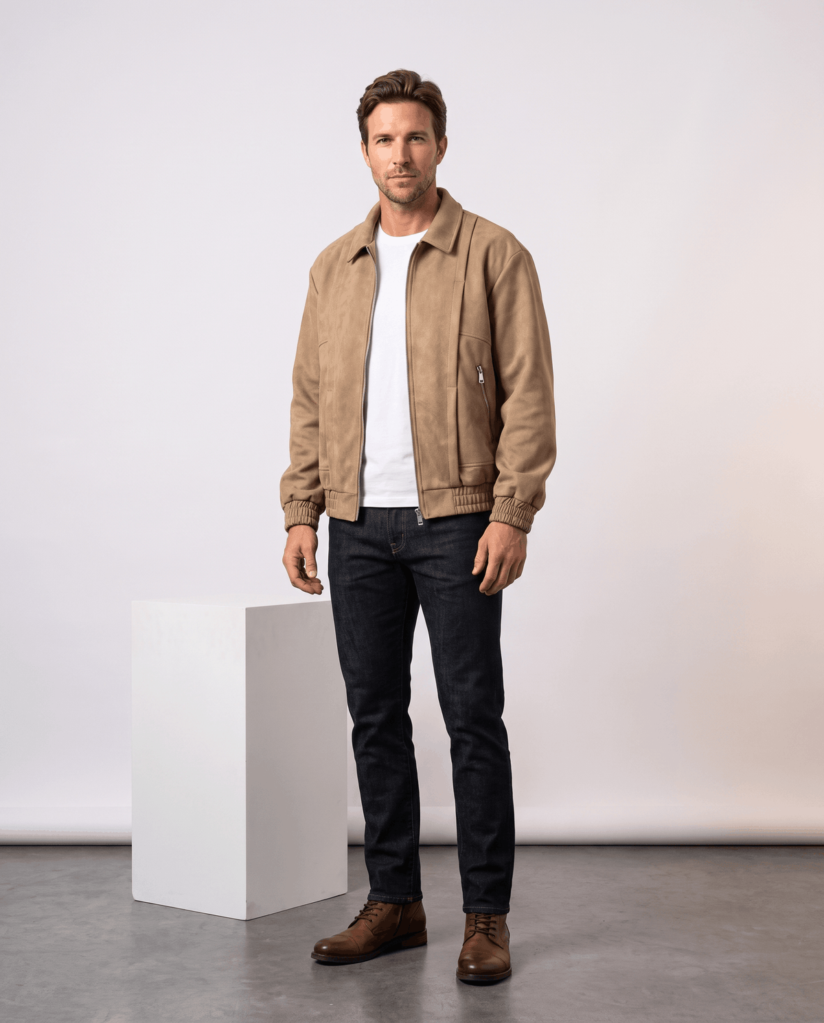 A man wearing a tan suede bomber jacket with a relaxed fit and zip pockets, standing indoors
