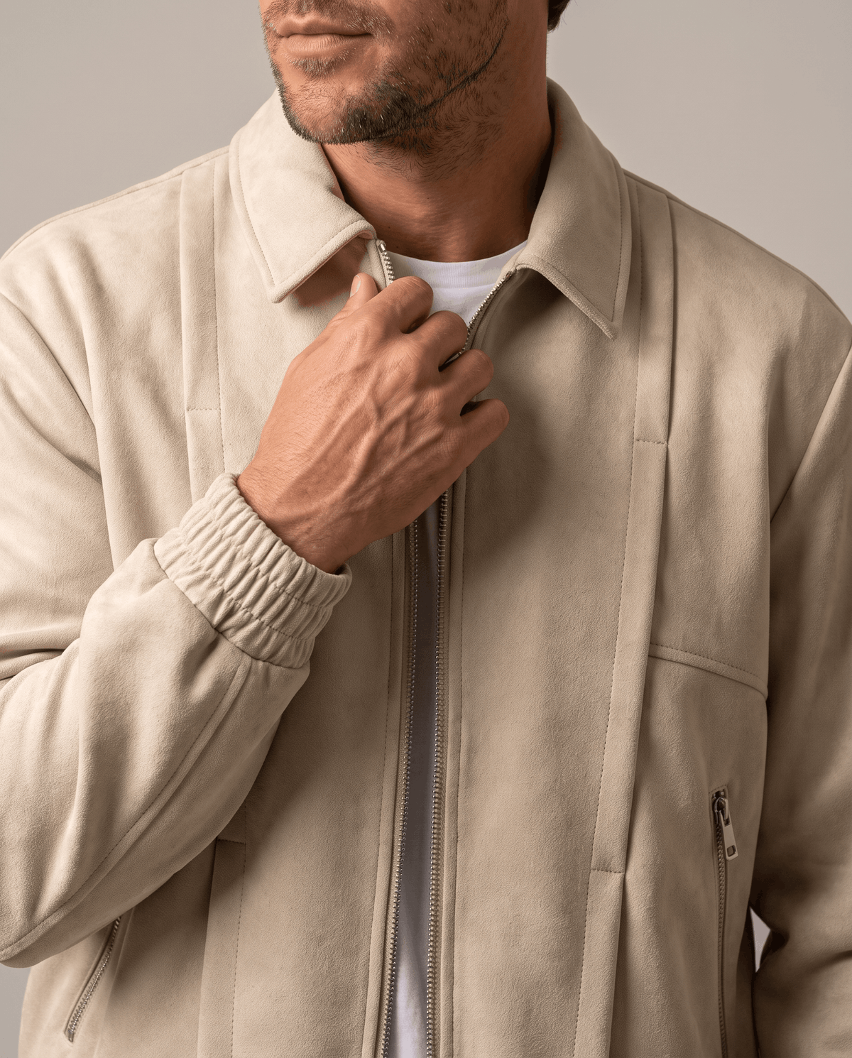 A man wearing a cream suede bomber jacket with a relaxed fit and zip pockets, shown adjusting the front