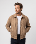 A man wearing a brown suede bomber jacket with a relaxed fit, zip pockets, and stand collar