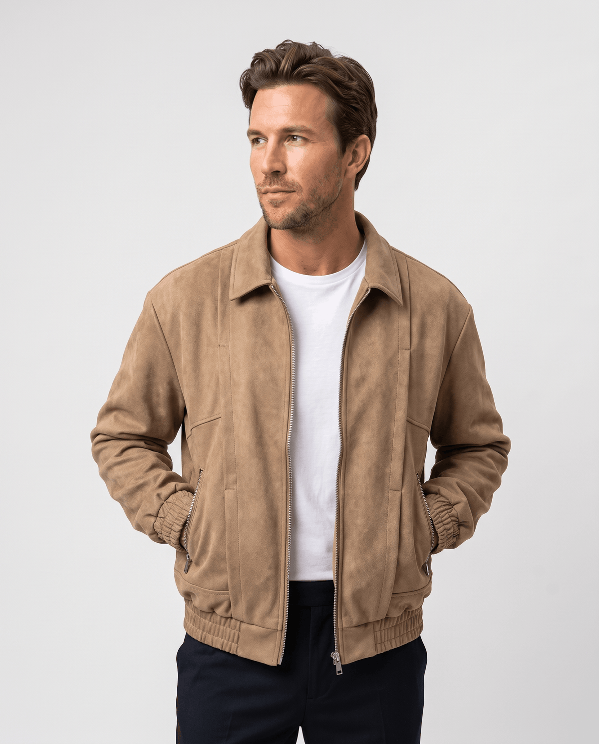 A man wearing a brown suede bomber jacket with a relaxed fit, zip pockets, and stand collar