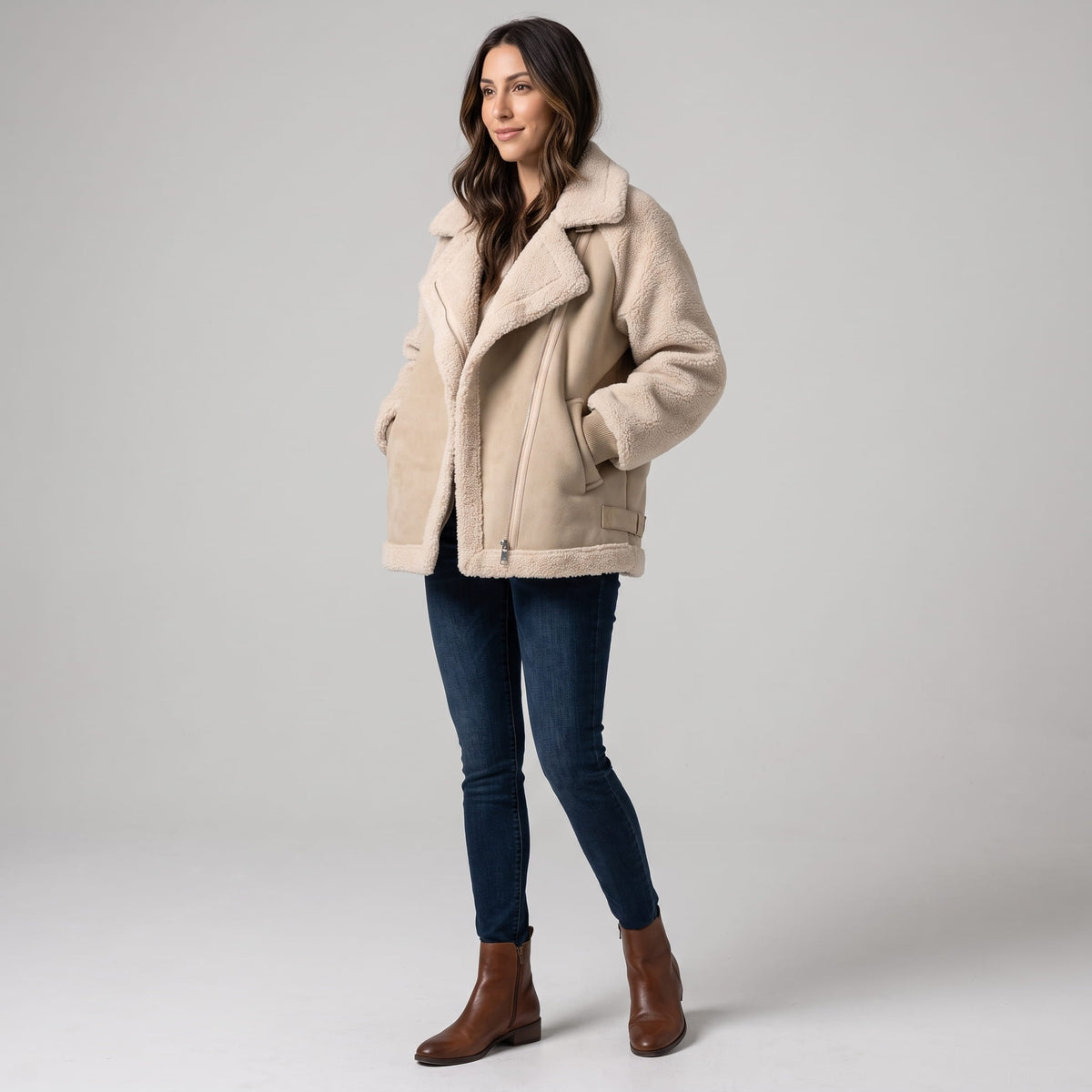 A woman wearing a beige suede leather shearling aviator jacket with an oversized lapel and sherpa trim, shown in side view