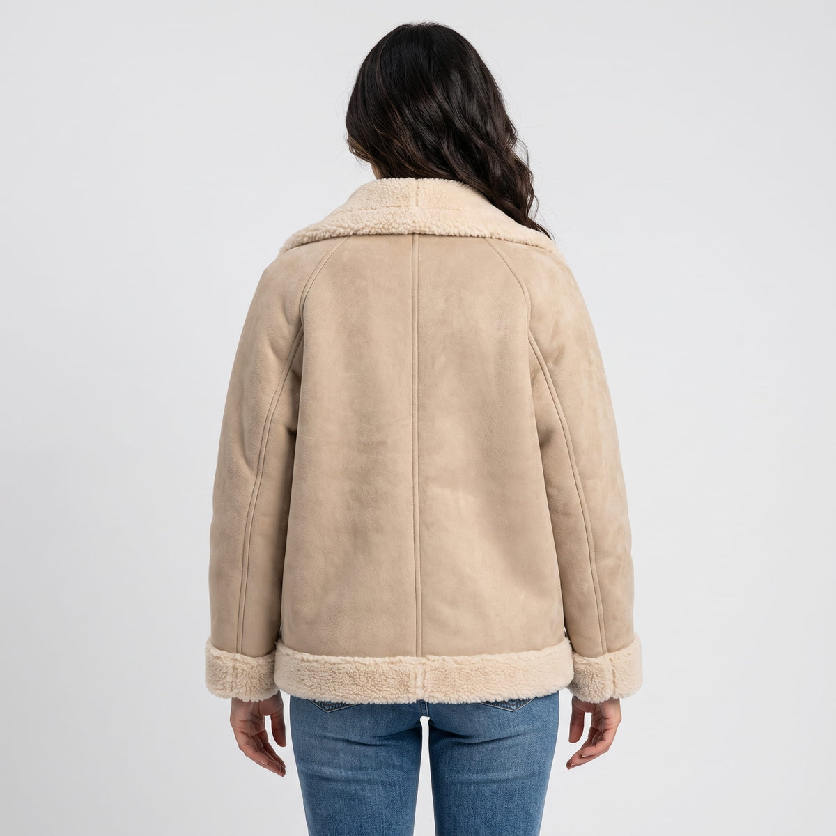 A woman wearing a beige suede leather shearling aviator jacket with an oversized lapel and sherpa trim, shown from the back