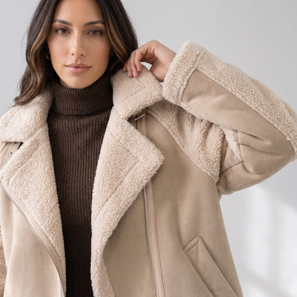 Close-up of a woman wearing a beige suede leather shearling aviator jacket, showing the oversized lapel and sherpa trim